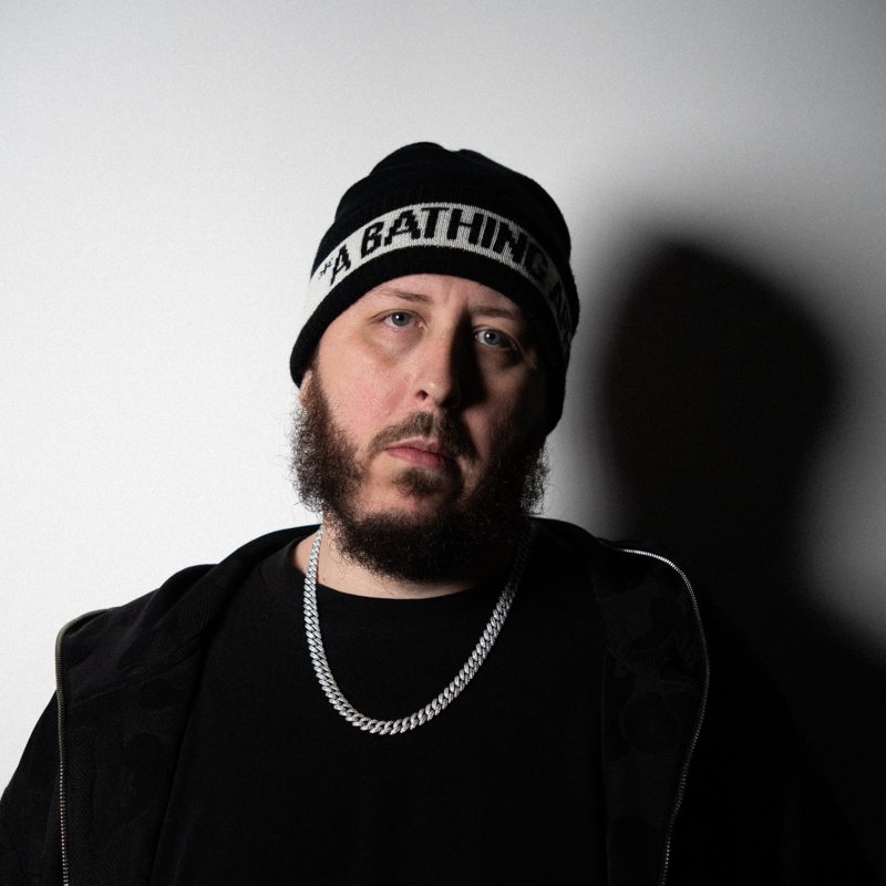Fenix in a black beanie and chain, his shadow on the white wall